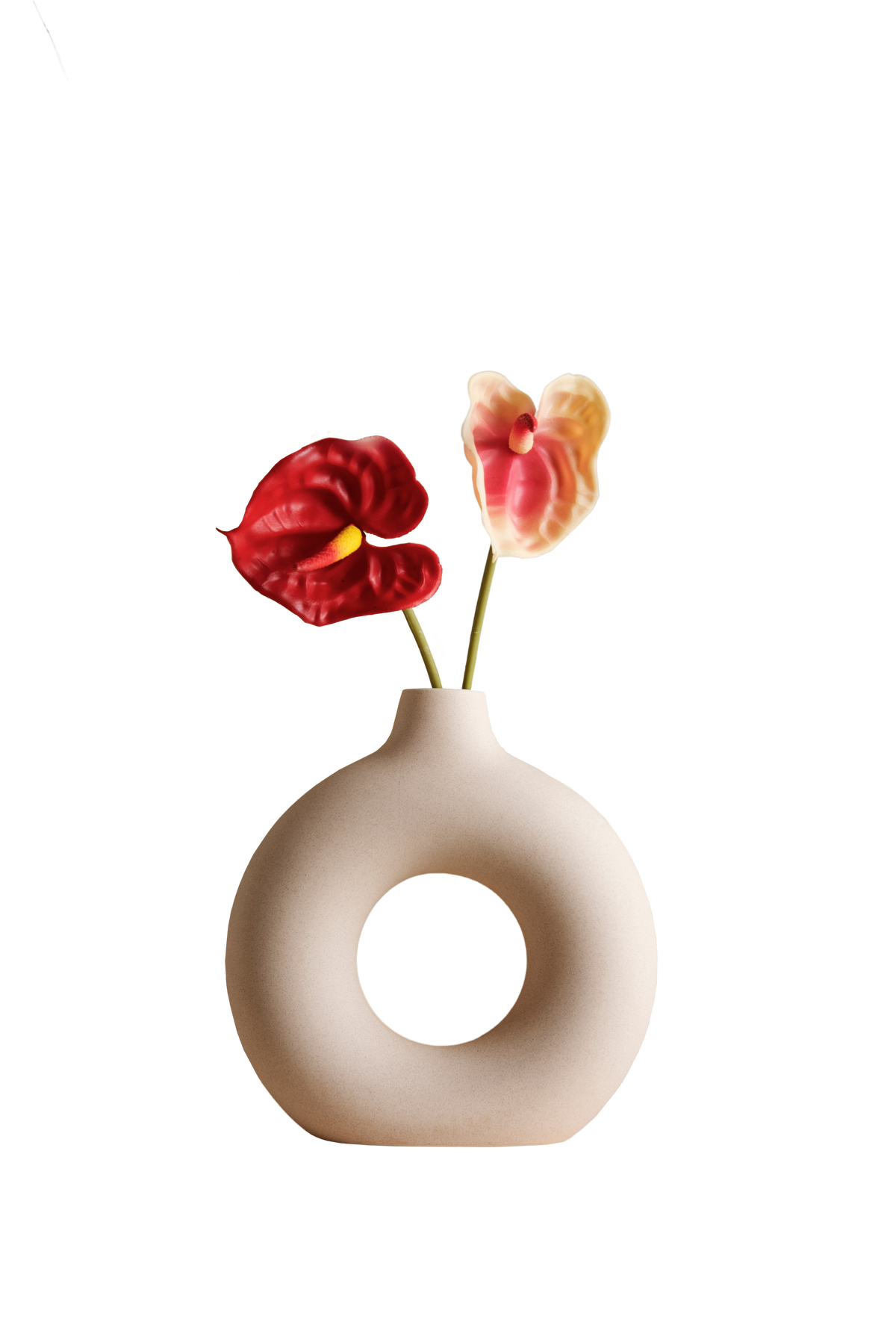 A minimalist beige ceramic vase with a central hole, holding two artificial flowers, one red and one pink and yellow, on a solid white background.
